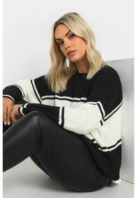 Virkat tröja med svart och vit rand, ribbad textur och avslappnad passform. Kombinerad med svarta leggings i konstläder.