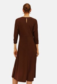 Braunes Midi-Kleid mit Dreiviertelärmeln, einem Schlüssellochdetail hinten und einem ausgestellten Rock. Hergestellt aus einem glatten, leichten Stoff.