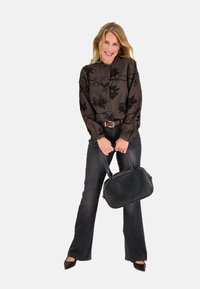 Zwarte blouse met bloemenprint en knoopsluiting aan de voorkant, gecombineerd met donkere jeans. Het model draagt een gestructureerde zwarte handtas en puntige hakken.