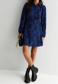 Abito a stampa leopardata blu e nera con maniche lunghe e collo a camicia, abbinato a stivali ankle neri con suola spessa e una borsa nera.