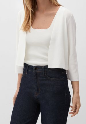 Femme portant un cardigan court blanc sur un haut blanc à encolure carrée, associé à un jean taille haute bleu foncé.