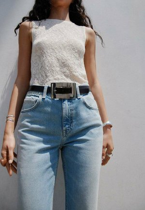 Spetslinne i off-white, parat med högmidjade ljusblå jeans och ett svart bälte med en glänsande silverspänne.