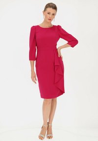 Fuksjowa sukienka z rękawami 3/4 typu puff, dopasowana sylwetka, szczegół z falbaną po bokach i gładka tekstura. Srebrne sandały na kostkę.