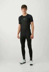 Black cycling bib shorts with short sleeves and straps, featuring a subtle logo detail. Made of stretchy, smooth material with body-hugging fit.