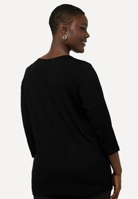 Schwarzes Langarmshirt aus einem weichen Stoff, mit rundem Ausschnitt und lässiger Passform, mit Nahtdetails auf der Rückseite.