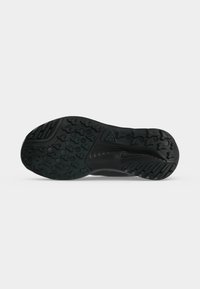 Semelle de chaussure en caoutchouc noir avec des motifs de bande de roulement texturés, des formes hexagonales et en étoile, et un logo intégré près de la zone de la voûte plantaire.