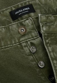 Pantalones de tela verde con una superficie texturizada, dos botones de metal y una etiqueta que dice "JACK & JONES JEANS INTELLIGENCE."