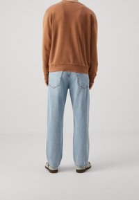 Felpa marrone con scollo tondo e polsini a costine abbinata a jeans denim blu larghi con doppie tasche posteriori. Sneakers con righe.