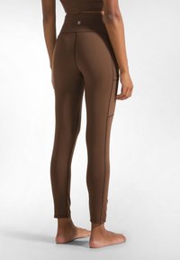 Leggings marroni a vita alta con cuciture piatte e tasche laterali, realizzati in materiale elasticizzato, progettati per il movimento attivo.