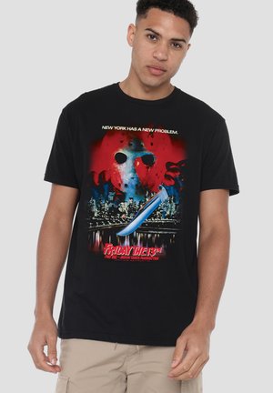 Young man wearing black t-shirt with graphic of a hockey mask, a large knife, and a city skyline with "Friday the 13th" text.