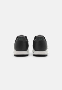 Baskets noires avec un dessus en cuir et en mesh, semelle intermédiaire blanche, semelle extérieure en caoutchouc noir texturé et logo vert brodé au talon.