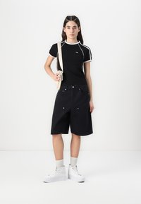 Svart kortärmad skjorta med vita detaljer, i kombination med svarta denimshorts. Vita högklackade sneakers och en beige axelväska fulländar looken.