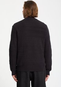 Mørk strikket sweater med et tekstureret mønster og vandrette striber, ribbede manchetter og kant, lavet af blødt stof.