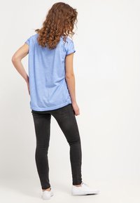 Hellblaues T-Shirt mit kurzen Ärmeln und abgerundetem Saum, kombiniert mit schwarzen Skinny-Jeans und weißen Sneakers, von hinten betrachtet.