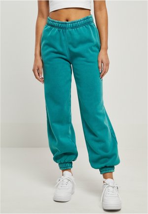 Person wearing teal elastic waist and ankle jogger pants with white sneakers against a plain background.