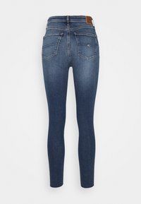 Jean en denim foncé, coupe ajustée, avec une texture lisse, poches arrière discrètes et une étiquette en cuir marron à la taille.