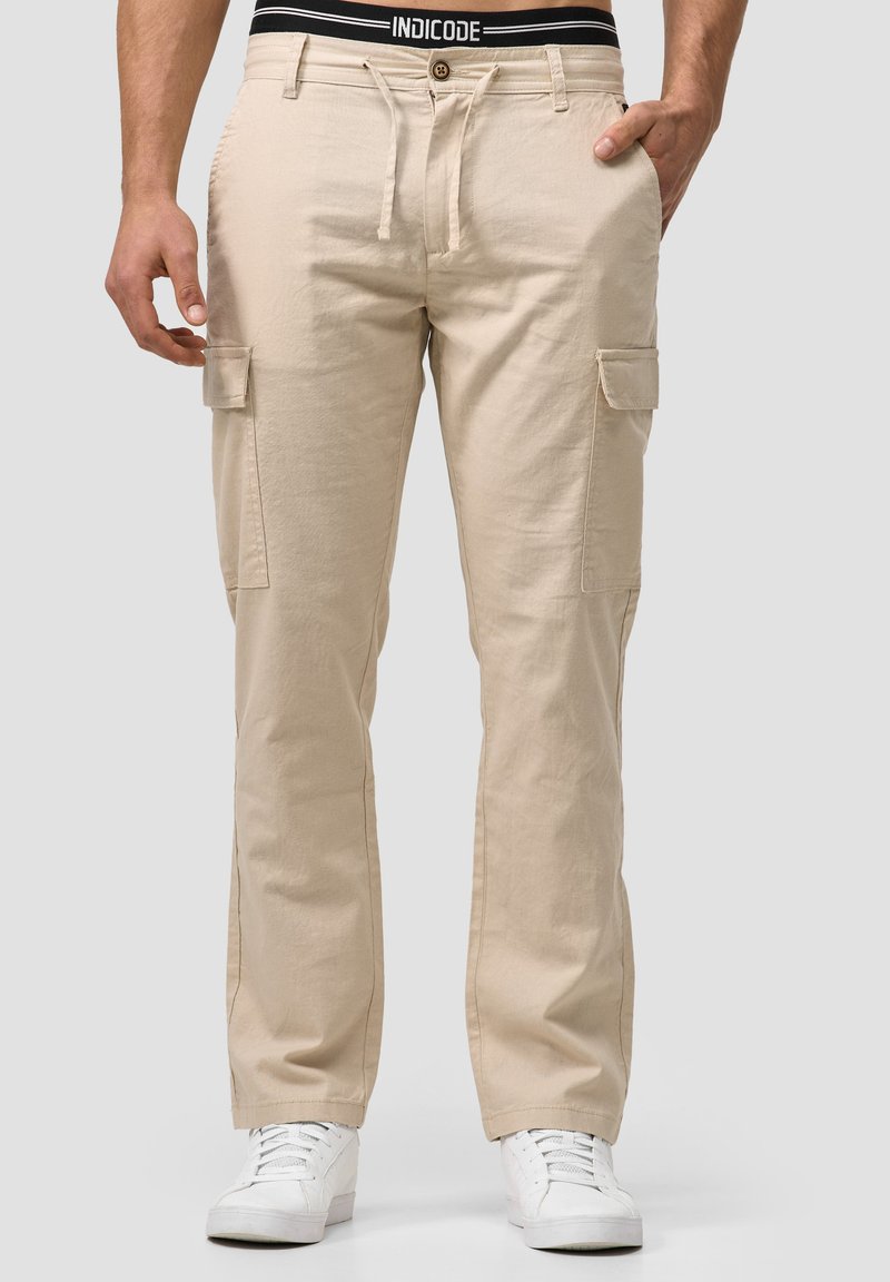 Beige cargo hlače s remenom u struku, s bočnim džepovima i glatkim, laganim materijalom. Nosene s bijelim tenisicama.