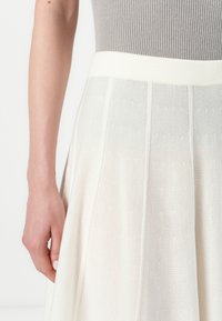 Hvit strikket skjørt med ribbestrikket midje, med teksturerte vertikale striper og subtile prikkemønstre, som viser et lett og flytende design.