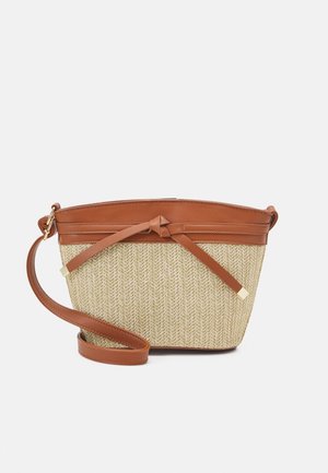 Sac bandoulière avec corps beige tissé et garniture en cuir marron, sangle et détail décoratif en nœud sur fond blanc uni.