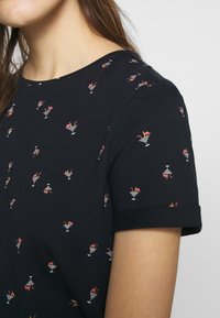 T-shirt noir à manches courtes avec un motif répété de cocktails, accents roses et verres rayés blancs. Tissu en coton doux et lisse.