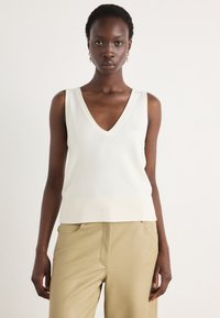Top sans manches crème en V avec ourlet et encolure côtelés, confectionné dans un tissu en maille lisse, assorti à un pantalon beige ajusté.