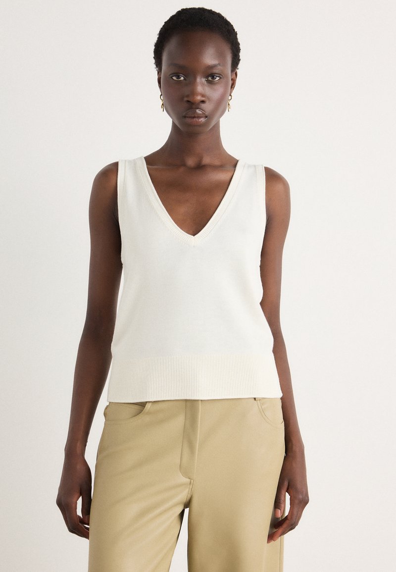 Top sans manches crème en V avec ourlet et encolure côtelés, confectionné dans un tissu en maille lisse, assorti à un pantalon beige ajusté.