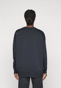 Felpa Nike grigia scura con scollo rotondo, maniche lunghe e polsini a costine. Presenta un logo discreto sulla schiena vicino alla spalla.