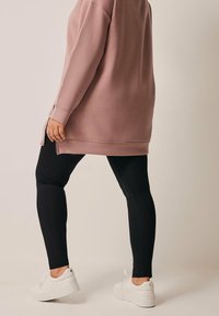 Overmaat roze sweatshirt met lange mouwen en zijsplitten, gedragen met zwarte leggings en witte gemarmerde platform sneakers.