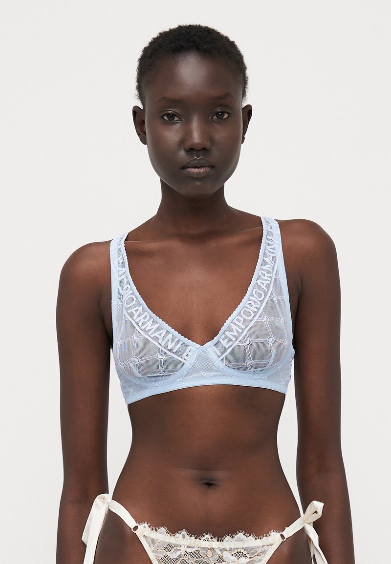 Bralette in pizzo azzurro chiaro con scollatura a V e spalline larghe, caratterizzato da un ampio elastico con logo. Texture trasparente con motivo geometrico.