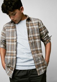 Brun och grå rutig skjorta med uppkavlade ärmar och knäppt fram, över en ljusgrå t-shirt. Svarta byxor. Subtila strukturer och mönster.