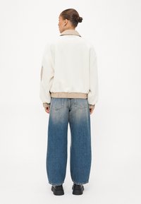 Crème-kleurige fleecejas met een beige kraag en manchetten, gecombineerd met lichtblauwe wijde denim jeans. Soepele textuur en een relaxte pasvorm.