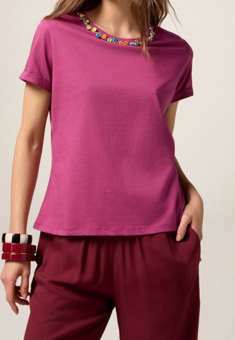 T-shirt fuchsia à manches courtes avec revers, orné d'une broderie florale autour du col. Matière en coton doux.