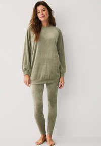 Completo loungewear verde oliva realizzato in morbido tessuto peluche. Presenta una maglia a maniche lunghe con scollo rotondo e leggings aderenti.