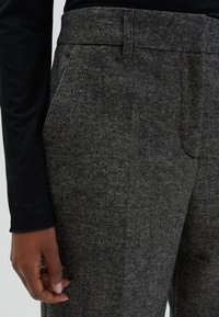 Grijze, getextureerde broek met een op maat gemaakte pasvorm, voorzien van zijzakken en een gladde tailleband, gecombineerd met een zwart, lange mouwen top.