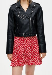 Veste de moto en cuir noir avec des accessoires en métal argenté, dotée de fermetures éclair et d'une taille ceinturée, associée à une robe à motif floral rouge.