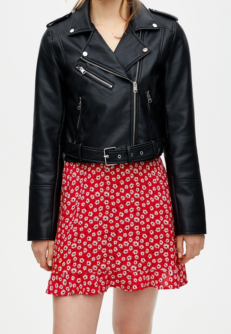 Veste de moto en cuir noir avec des accessoires en métal argenté, dotée de fermetures éclair et d'une taille ceinturée, associée à une robe à motif floral rouge.