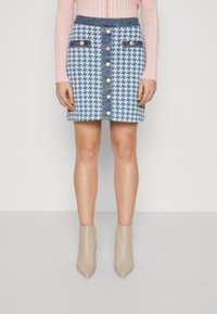Jeansminiskjørt med et blått og hvitt houndstooth-mønster, med frontknapplukking og dekorative lommer, sammen med beige ankelstøvler.