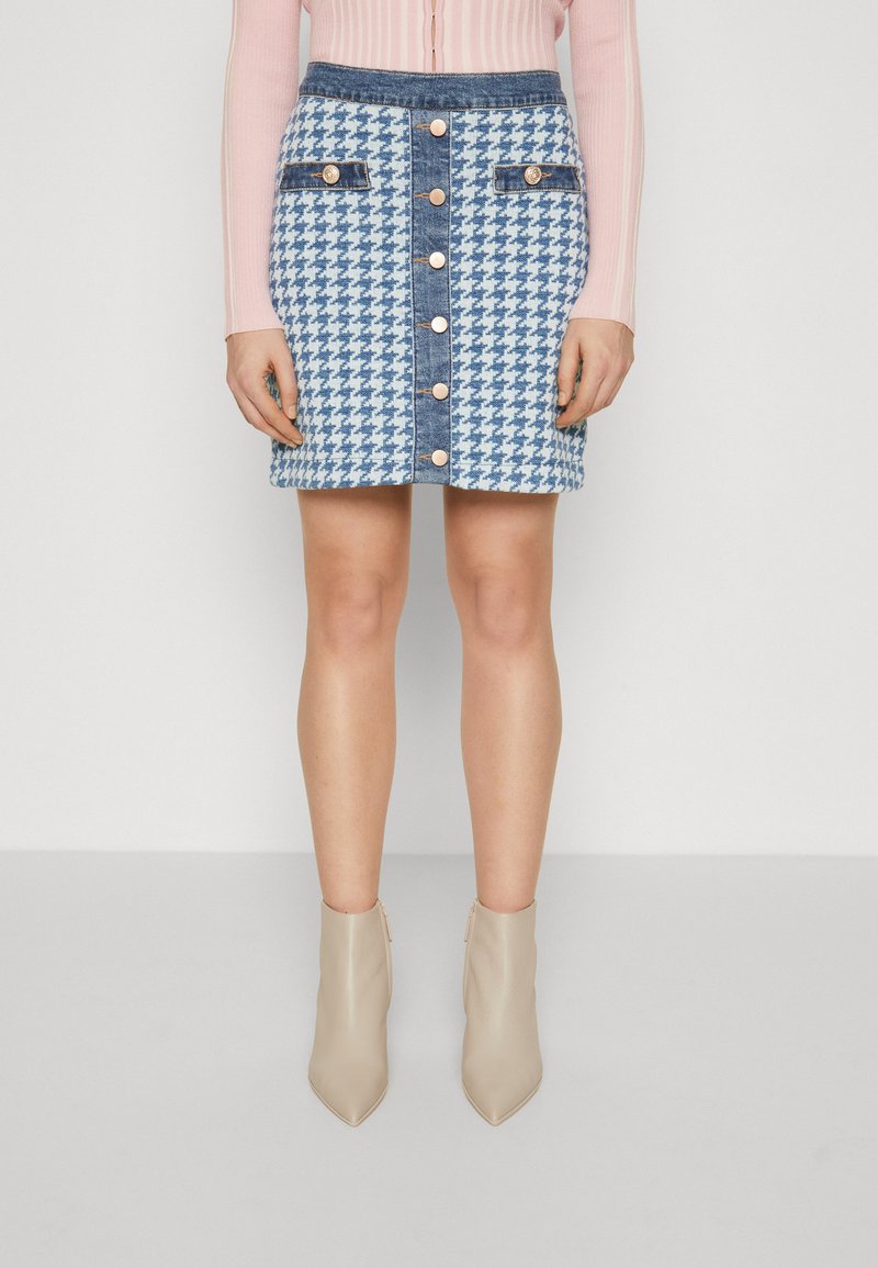 Jeansminiskjørt med et blått og hvitt houndstooth-mønster, med frontknapplukking og dekorative lommer, sammen med beige ankelstøvler.