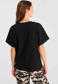 Camiseta negra de manga corta con un corte relajado y puños enrollados, hecha de una tela suave, combinada con pantalones beige con estampados.