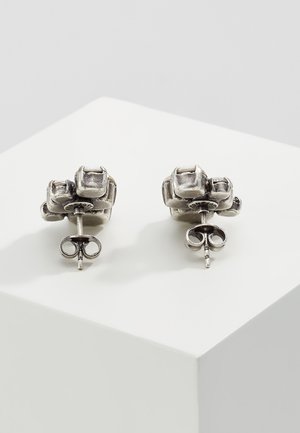 Paar silberner Ohrstecker mit strukturierten, gruppierten quadratischen Designs, von hinten auf einer weißen schrägen Oberfläche gezeigt.