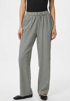 Kobieta w luźnych, czarno-białych pionowo paskowanych spodniach z wysokim stanem, elastycznym pasem i czarnych balerinach.