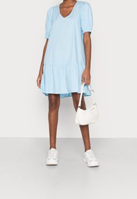 Světle modré bavlněné šaty s nabíranými rukávy, výstřihem do V a vrstvenou sukní. Kombinováno s malou bílou kabelkou a bílými teniskami.