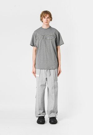 Camiseta gris de manga corta con logo, combinada con pantalones de chándal grises, con cordón y bolsillos laterales, completada con calzado negro texturizado.