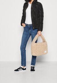 Czarna kurtka puchowa, biała bluzka, niebieskie dżinsy, czarne sneakersy z białymi akcentami oraz beżowa, puszysta torebka na krótkich rączkach.