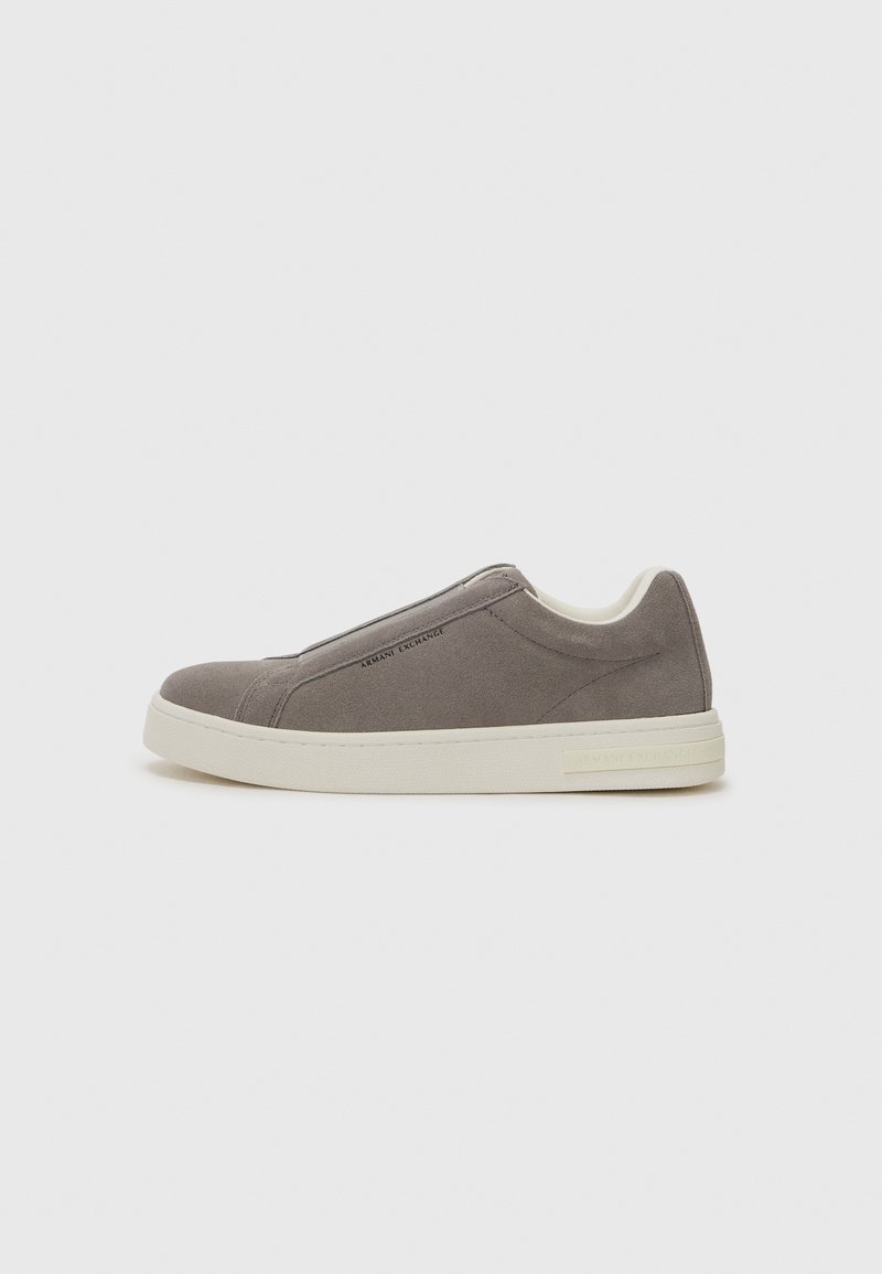 Sapatilha slip-on em camurça cinza com sola de borracha creme, apresentando um acabamento suave e uma marcação discreta na lateral. Design minimalista.