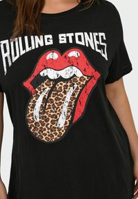 Czarny t-shirt z krótkim rękawem z wyblakłym graficznym wzorem czerwonych ust z językiem w panterkę. Tekst "Rolling Stones" w białym kolorze nad wzorem.