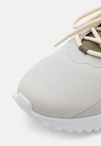 Sneaker beige chiaro con una parte superiore testurizzata, punta rotonda e suola bianca. Presenta lacci crema e un design di pannello sottile.