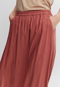 Roestkleurige wijde broek van zacht materiaal, met een elastische tailleband en zijzakken met een gladde structuur.