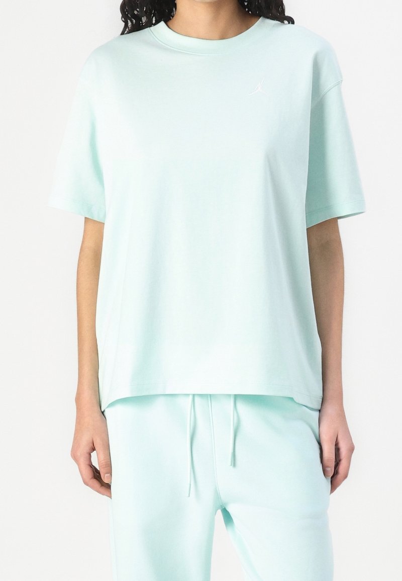 T-shirt oversize turquoise clair en coton doux, avec un col rond et des manches courtes. Un petit logo blanc est présent sur la poitrine.