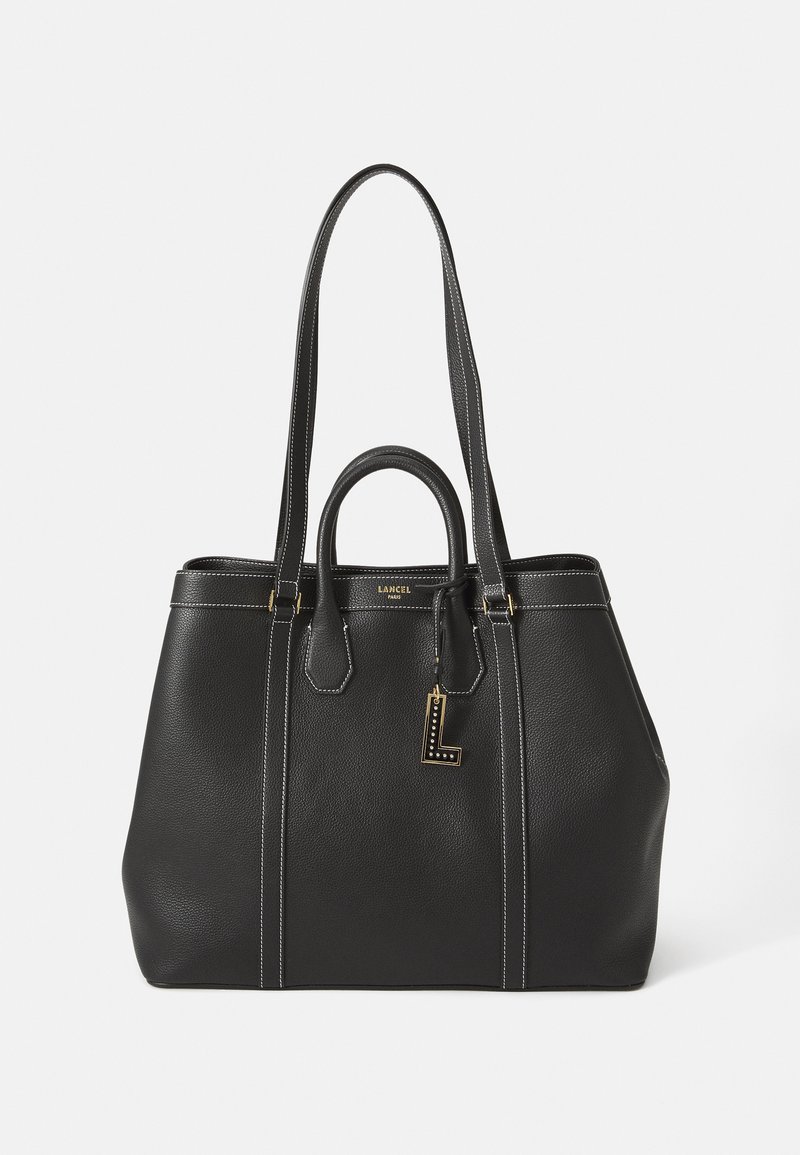 Saco de couro preto com alças duplas, acabamentos em dourado e costura branca; inclui uma etiqueta decorativa com letra e forma estruturada.